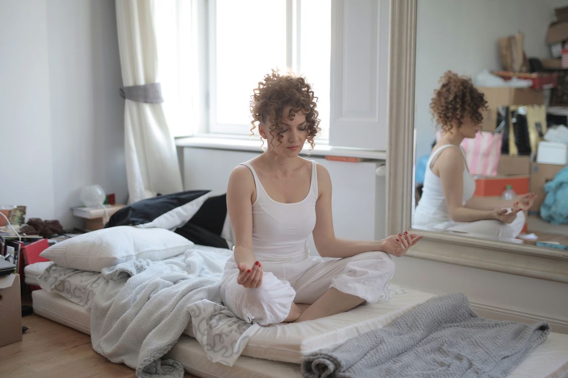 Mujer en posición de loto practicando meditación en su hogar, representando calma y bienestar interior